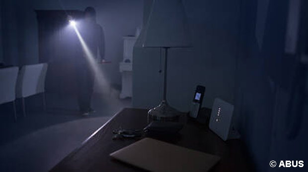Ein dunkel gekleideter Einbrecher läuft mit einer Taschenlampe durch eine Wohnung